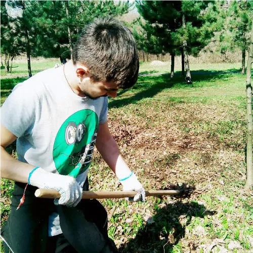 Man using a hoe to contact the soil in a forested area.